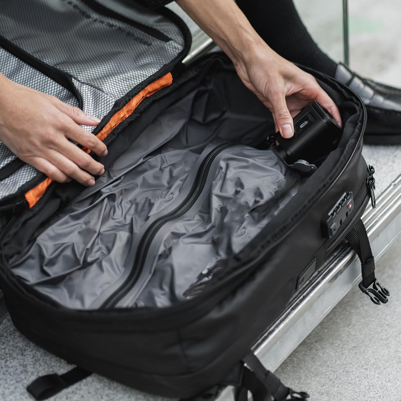 Person packing a black backpack with orange accents into a suitcase.